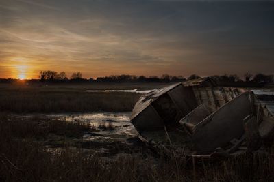 Abandoned boat on field against sky during sunset