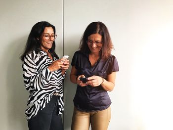 Smiling female friends using mobile phone while standing at home