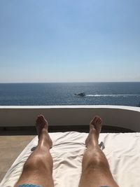 Low section of man relaxing on sea against clear sky