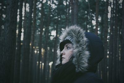 Side view of young woman wearing fur hood against trees at forest