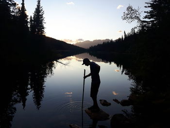 Silhouette man standing on rock in lake against sky during sunset