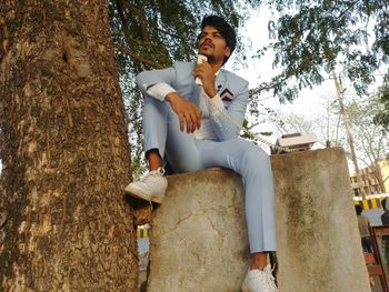Low angle view of man using mobile phone while sitting on tree