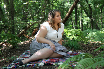 Young woman sitting on blanket amidst trees in forest