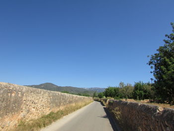 Road amidst trees against clear blue sky