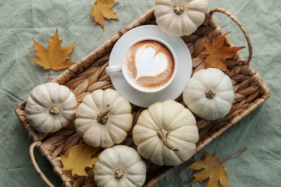 White pumpkins, coffee and autumn leaves on a wicker tray. autumn home decor.