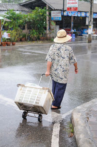 Rear view of man with shopping cart on wet street