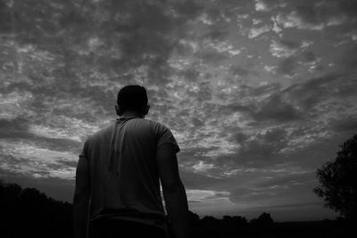 Rear view of silhouette man standing against cloudy sky