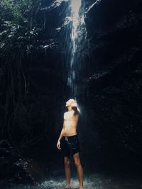 Man standing under waterfall in forest