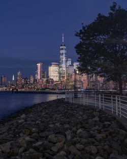Illuminated buildings by trees against sky in city