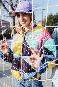 Female clutching the fence wearing a multicolored jacket