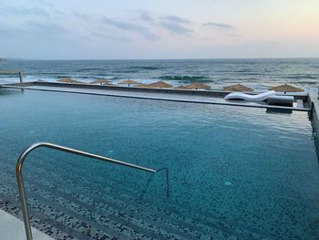 Swimming pool by sea against sky during sunset