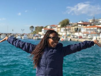 Happy woman standing with arms outstretched against sea in city