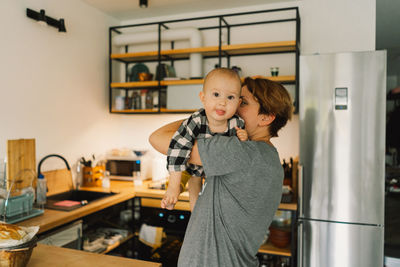 A mother holds her daughter in her arms in the kitchen.