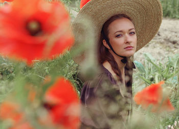 Portrait of young woman wearing hat while standing in park among poppies flowers