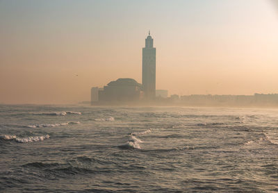 Lighthouse by sea against sky during sunset