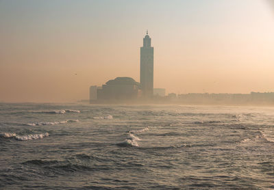 Hassan ii mosque by sea against sky during sunset