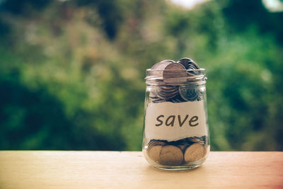 Close-up of jar with coins and save message on table