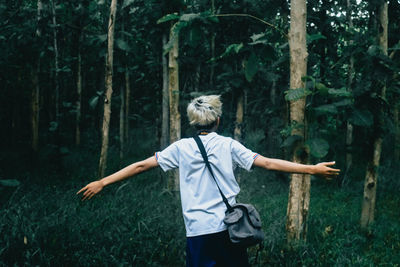 Rear view of woman standing by tree in forest