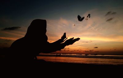 Silhouette person by sea against sky during sunset