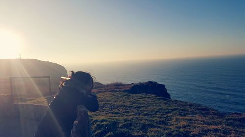 Woman standing on observation point looking at sea against clear sky during sunny day