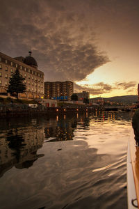 Buildings by river against sky at dusk