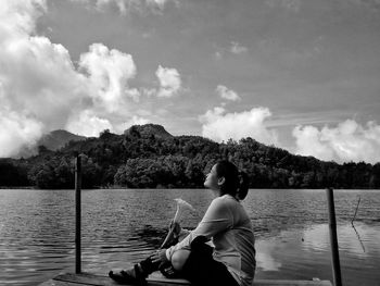 Full length of woman sitting by lake against sky