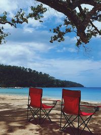 Deck chairs on beach against sky