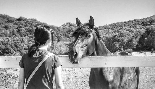 Rear view of girl standing in front of horse against clear sky