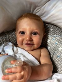 Portrait of cute baby boy holding milk bottle while lying down on bed