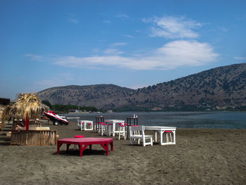 Chairs and tables on beach against blue sky