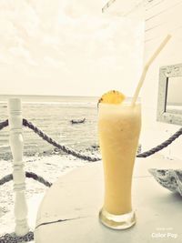 Close-up of drink on table by sea against sky