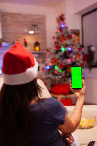 Rear view of woman holding christmas tree at home