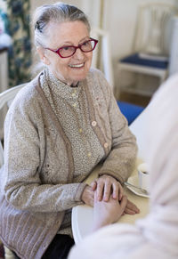 Smiling senior woman holding female home caregiver's hand at table