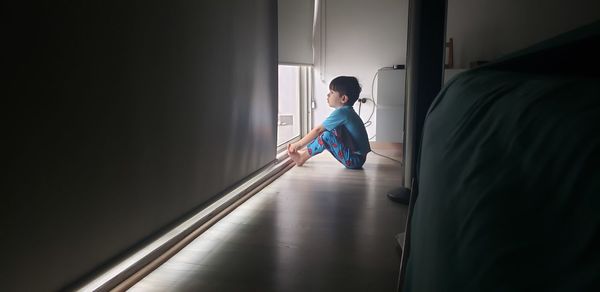 Side view of boy looking through window at home