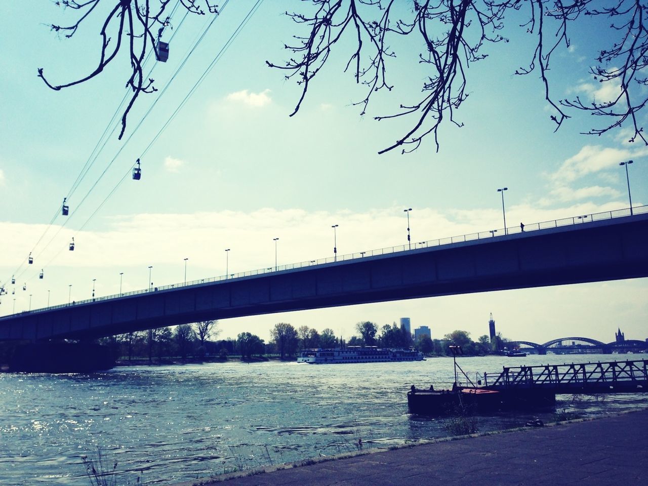 connection, bridge - man made structure, sky, water, river, built structure, architecture, cloud - sky, transportation, bridge, railing, tree, bare tree, cloud, nature, city, engineering, cloudy, waterfront, no people