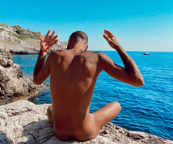 Rear view of shirtless man at beach against sky