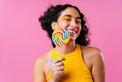 Portrait of young woman holding lollipop against coral background