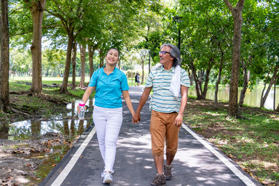 Couple holding hands while walking on road against trees in park