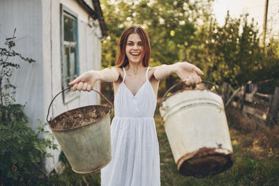 Smiling woman holding buckets while standing outdoors