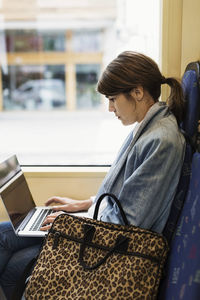 Side view of young woman using laptop in tram