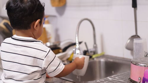 Rear view of boy with faucet in water at home