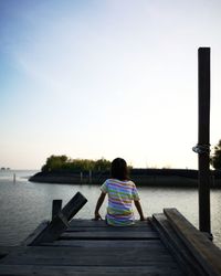 Rear view of woman sitting on pier over lake against sky