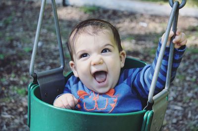 Portrait of cheerful boy sitting in swing at playground