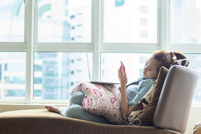 Midsection of woman using phone while sitting on window