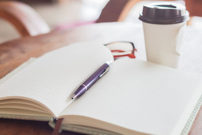 High angle view of book with pen and eyeglasses by coffee mug on table