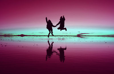Pop art styled silhouette of happy couple jumping on the mirror effect of uyuni salt flats, bolivia