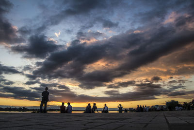 People at beach against cloudy sky during sunset