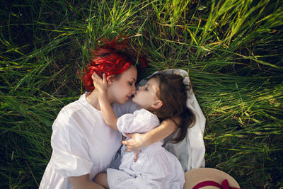 Girl a child hug mother mother with red hair lying on a green field at sunset