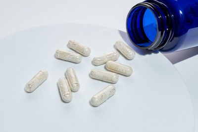 Close-up of pills spilling from bottle against white background