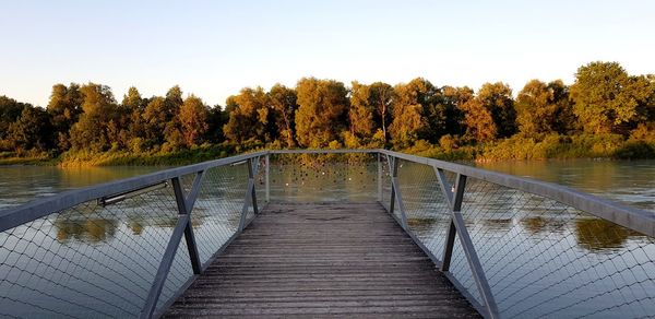 Footbridge over lake against clear sky